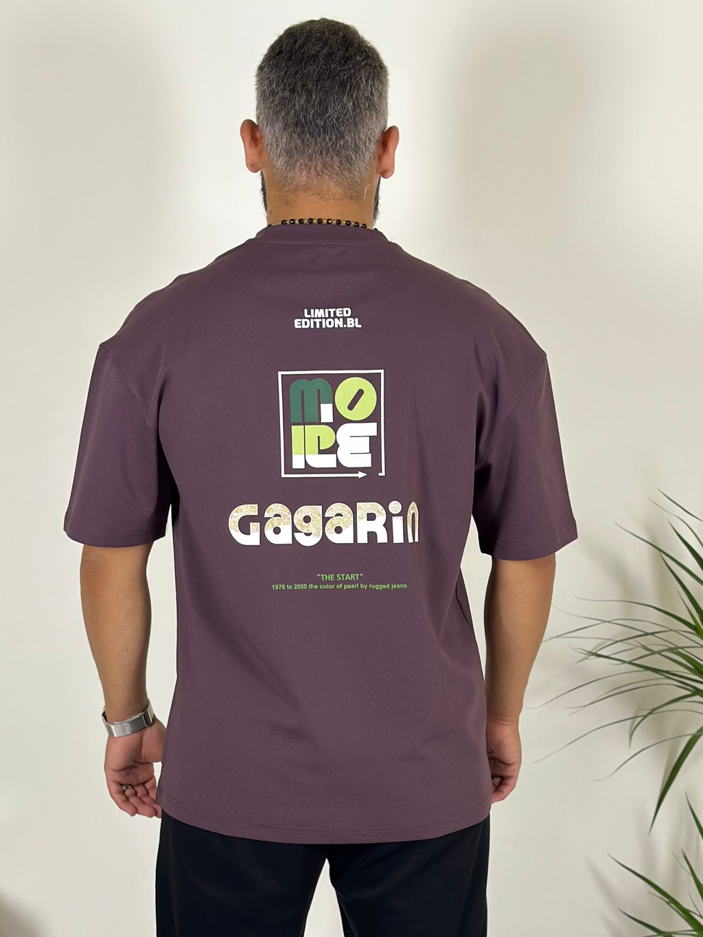 Man wearing a purple t-shirt with 'Gagarin' logo standing in a room with a plant.